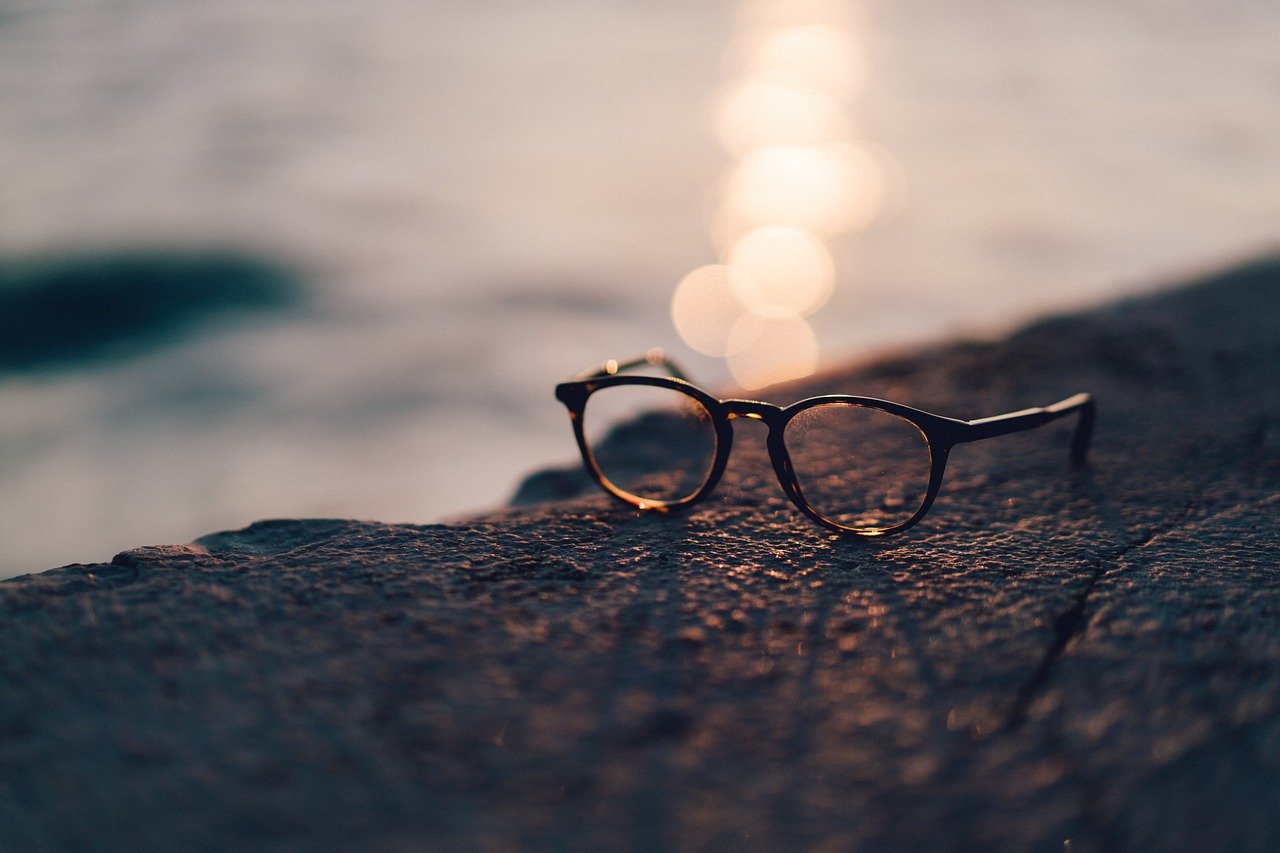 A pair of eyeglasses on a rocky cliff overlooking a body of water.
